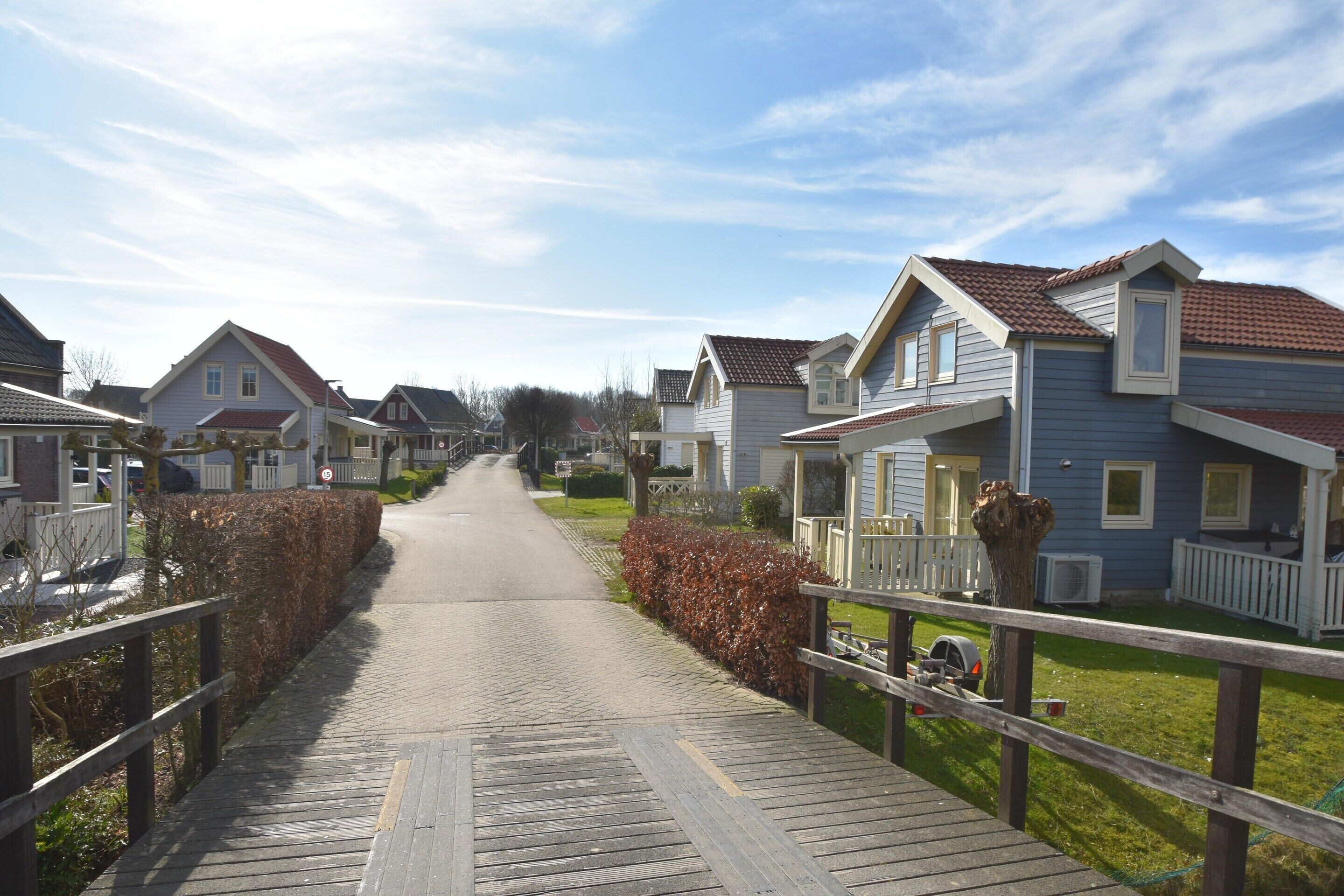 A residential street with houses, a wooden walkway, and a clear sky.
