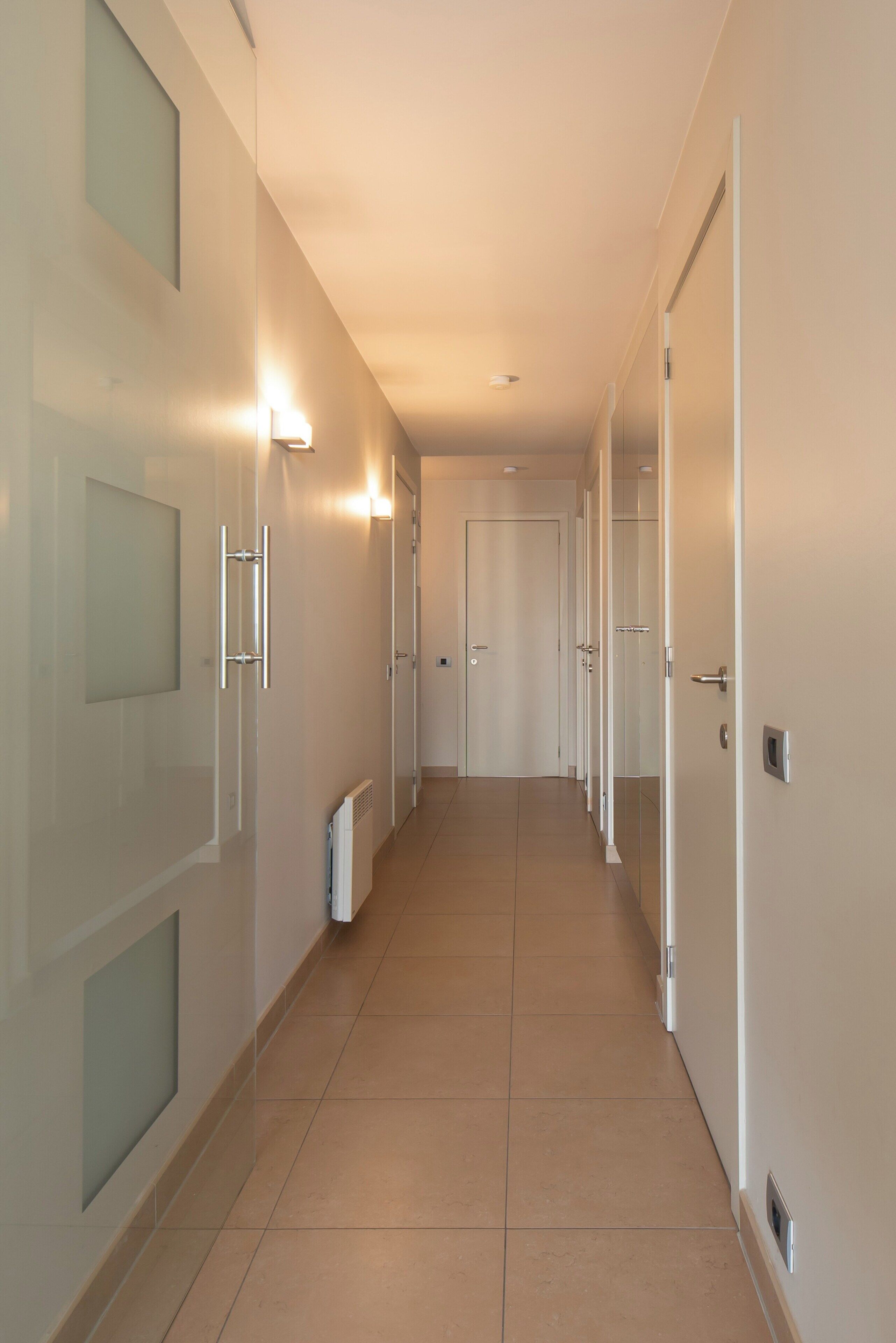 A long, narrow hallway with white walls and doors, leading to multiple rooms.