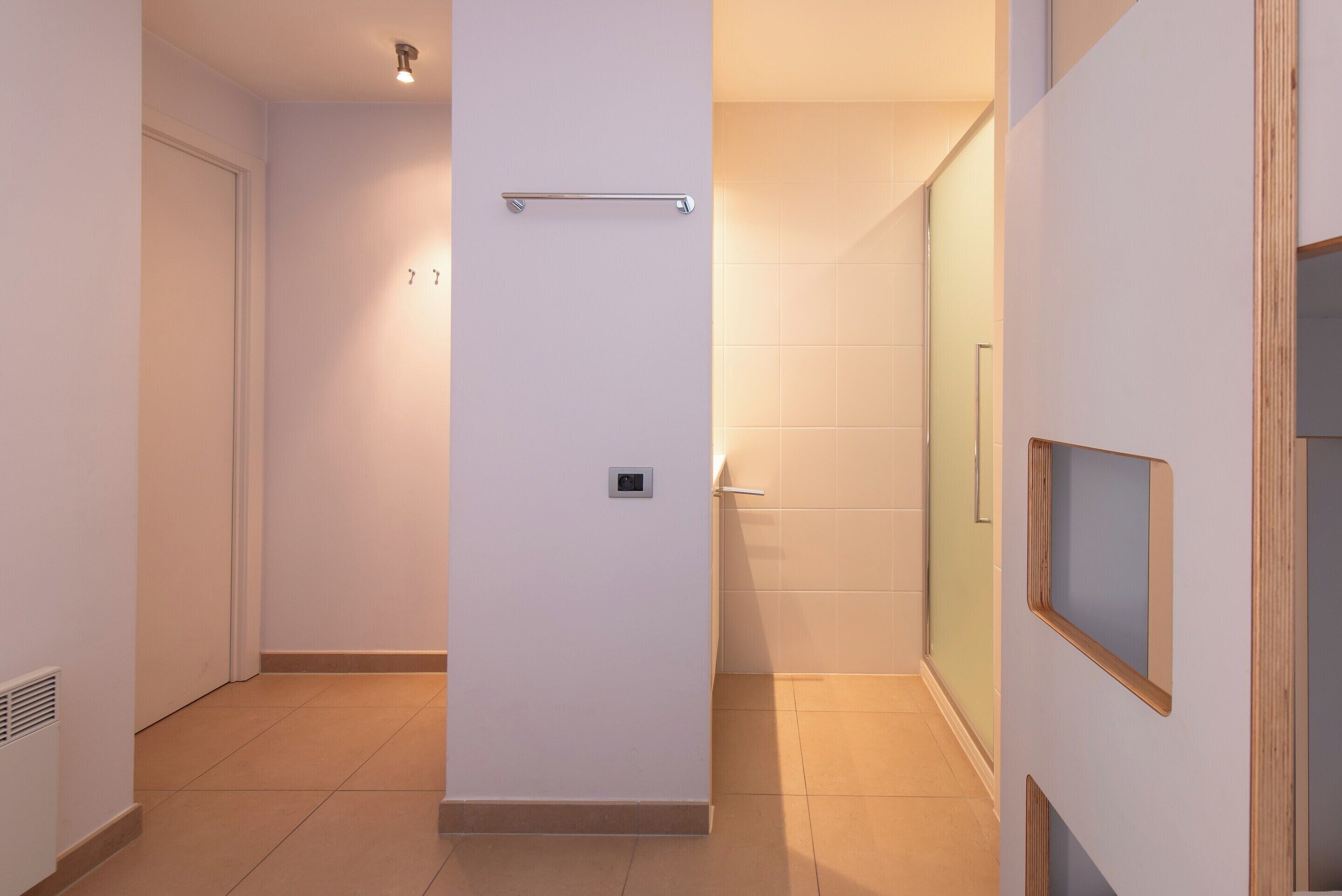 A hallway with a handrail, a door, and a glass shower enclosure.