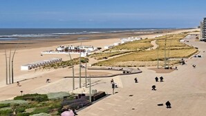 A coastal promenade with a beach, a row of white buildings, and a few people walking.