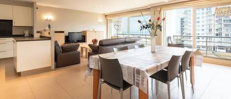 A modern apartment with a dining area, kitchen, living room, and balcony with a city view.
