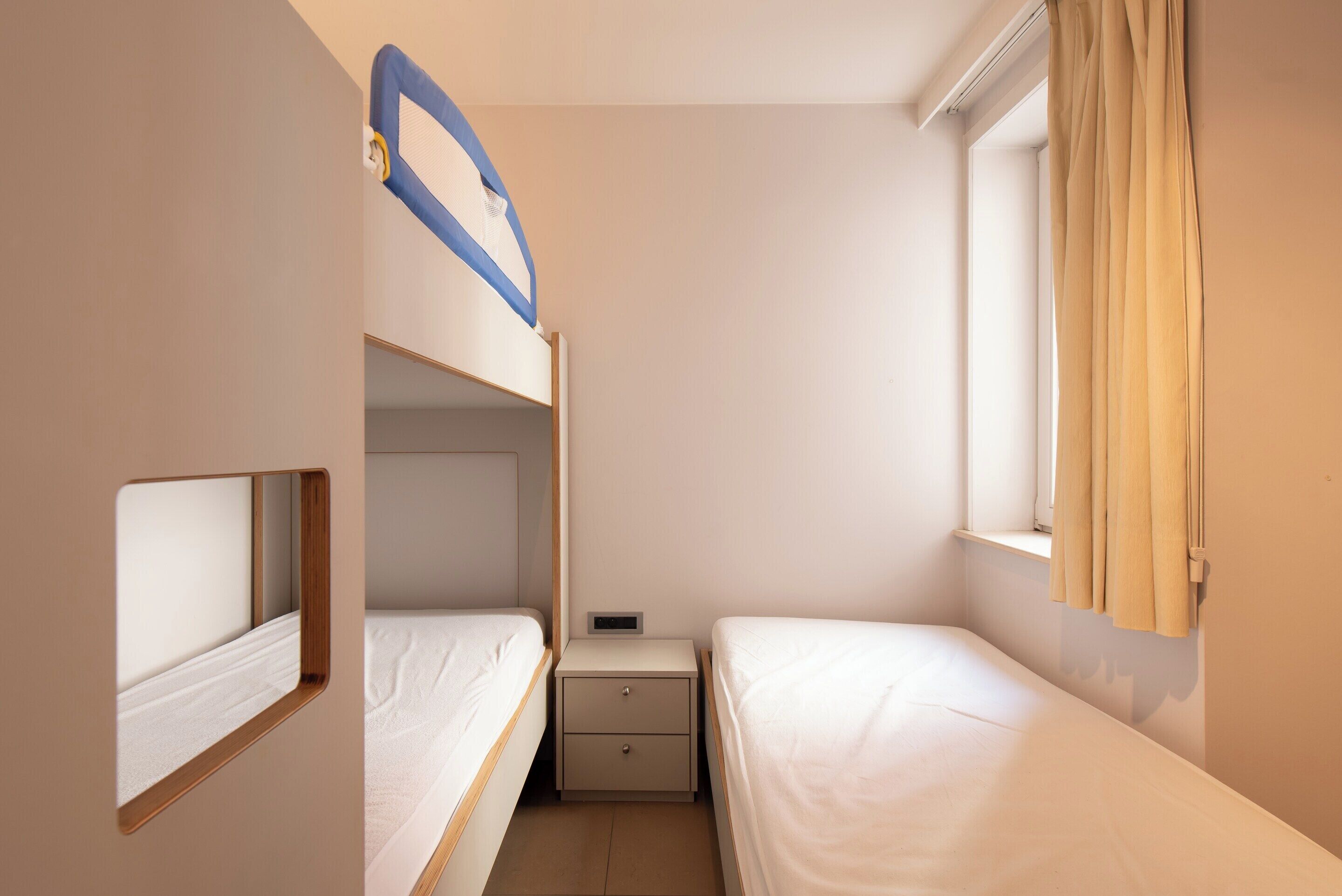 A small, compact room with two single beds, a nightstand, and a window with curtains.