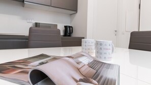 A modern kitchen with a white countertop, two grey chairs, and a magazine on the table. - Italianway - Pianell 5 A (Milan)