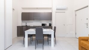 Una cocina compacta con una mesa y sillas blancas, microondas y cafetera.