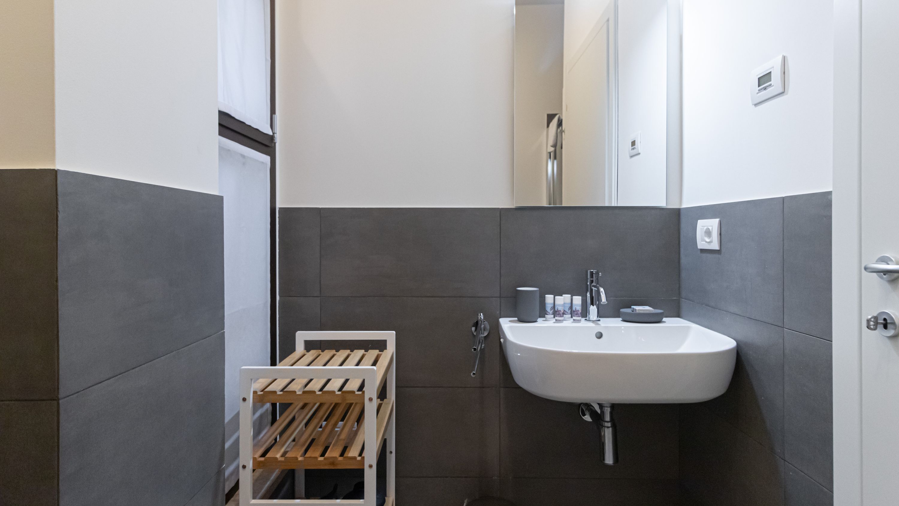 Une salle de bain moderne avec un lavabo blanc, des carreaux gris et un étendoir à linge en bois.