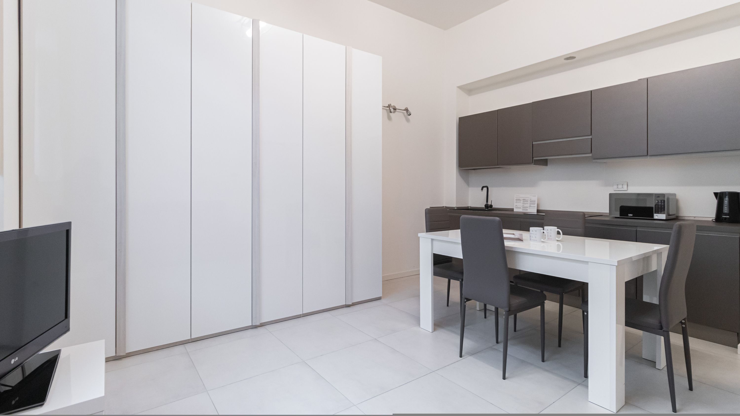 Una cucina moderna con zona pranzo, mobili bianchi e televisore a schermo piatto.