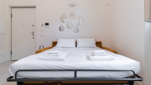 A neatly made bed with white linens and towels, a wooden headboard, and a wall-mounted thermostat. - Italianway - Pianell 5 A (Milan)