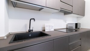 A modern kitchen with a black sink, stainless steel cabinets, and a microwave. - Italianway - Pianell 5 A (Milan)