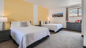 Habitación de hotel con dos camas, un aparador, una ventana con vistas y un cuadro en la pared.