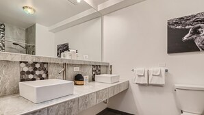Un baño moderno con un espejo grande, dos lavamanos, un inodoro y una ducha.