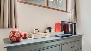 Una habitación con ventana, un escritorio con portavasos, un jarrón rojo y una tetera.