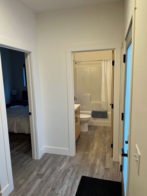 En smal gang, der fører til et badeværelse med bruser, toilet og håndvask.