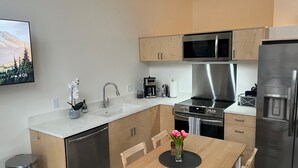 Eine moderne Küche mit Edelstahlgeräten, Holzschränken, einer Marmorarbeitsplatte und einem Essbereich mit Holztisch und Stühlen.