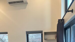 Ein modernes Wohnzimmer mit einem grauen Ecksofa, einem kleinen Beistelltisch und einem Fenster mit Blick auf ein Haus.