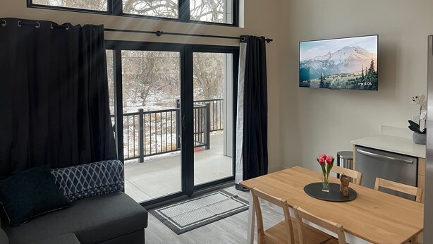 Ein modernes Wohnzimmer mit großem Fenster, einer Couch, einem Esstisch und einer Küchenzeile.