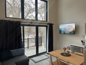 En moderne stue med et stort vindue, en sofa, et spisebord og et køkkenområde.