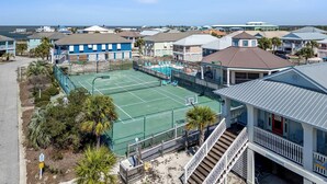A coastal residential area with a tennis court, beachfront houses, and a clear view of the ocean.