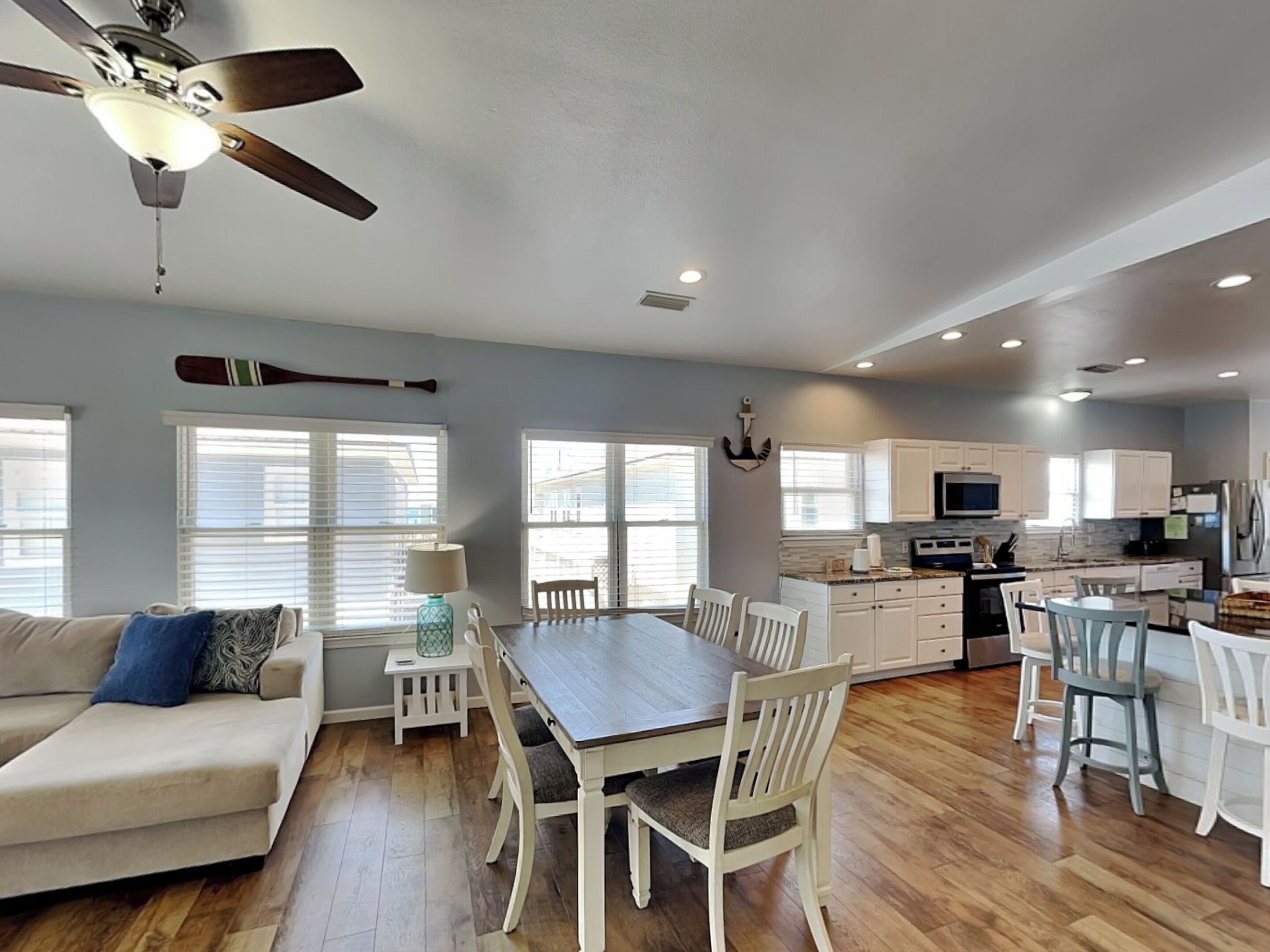 A spacious living area with a dining table, white furniture, a ceiling fan, and a kitchen with white cabinets and appliances.