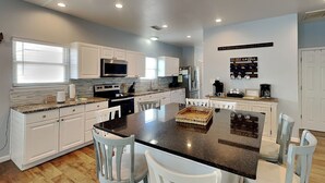 A modern kitchen with white cabinetry, granite countertops, and a central island with seating.