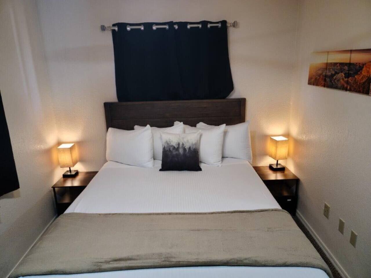 A neatly made bed with a wooden headboard, two bedside lamps, and a black curtain.