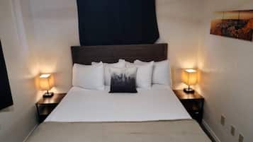 A neatly made bed with a wooden headboard, two bedside lamps, and a black curtain.