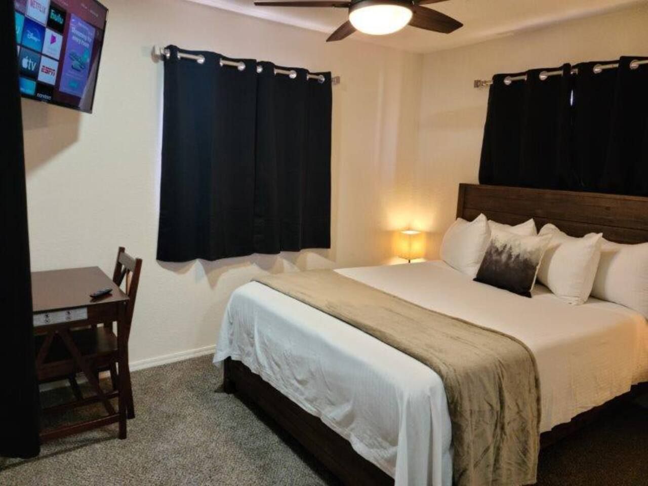 Quarto de hotel com uma cama, uma escrivaninha e uma televisão na parede.