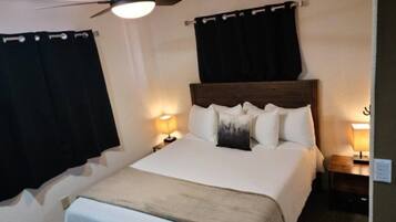 Ein Schlafzimmer mit einem großen Bett, zwei Nachttischen, einem Deckenventilator und schwarzen Vorhängen.