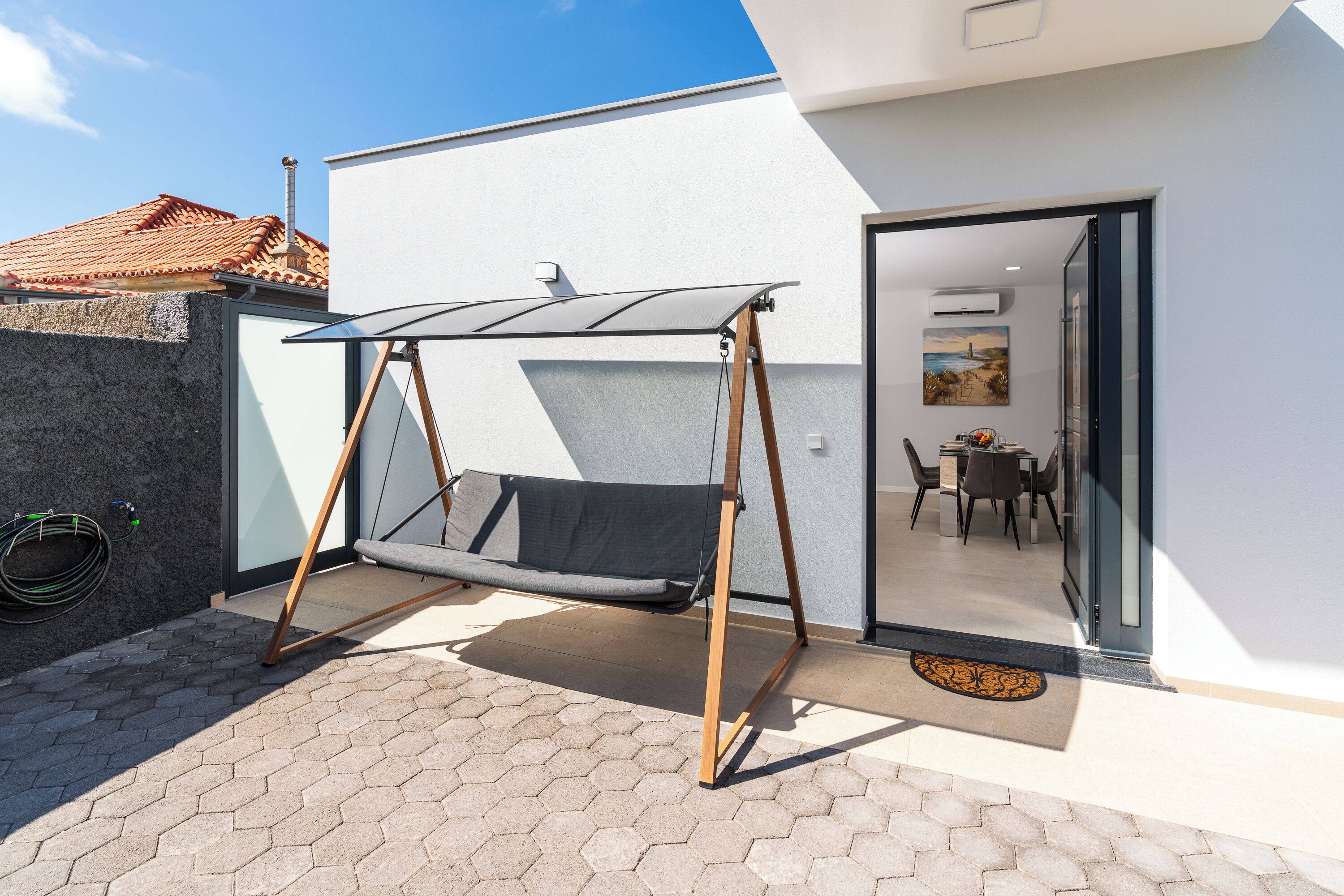 Un espace de détente extérieur moderne, doté d’une chaise suspendue, d’une terrasse carrelée et offrant une vue sur une salle à manger.