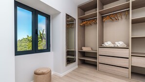 A walk-in closet with open shelves, a hanging rod, and a window with a view of greenery.