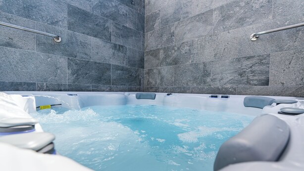 A modern bathroom with a large bathtub, grey stone tiles, and a metal grab bar.