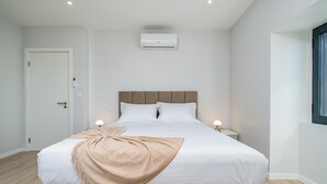 A modern bedroom with a large bed, bedside lamps, and a built-in air conditioning unit.