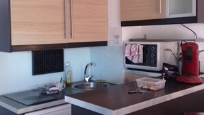 A compact kitchen with wooden cabinets, a stainless steel sink, a microwave, and a red coffee maker. - Lovely apartment near city center (Canet-en-Roussillon)