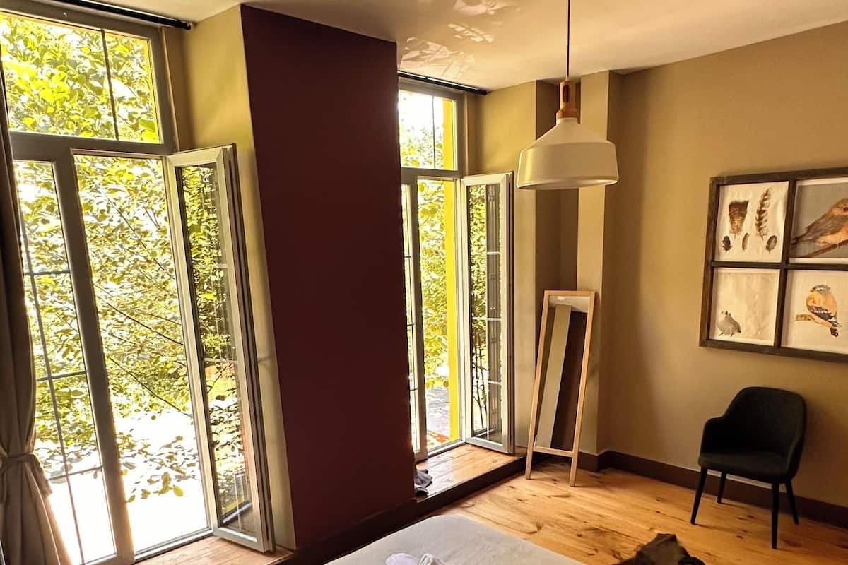 A hotel room with two beds, a large window, a ceiling fan, and a framed picture on the wall.