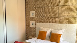 A hotel room with a patterned wall, a bed with white and orange pillows, a brown patterned bedspread, and a red towel on the bed. - Stylish Apartment - 5 Min Walk to Center (L'Isle-sur-la-Sorgue)