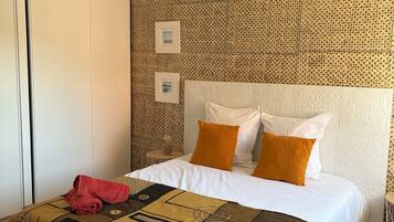 Une chambre d’hôtel avec un mur orné d’un motif, un lit avec des oreillers blancs et orange, une couverture de lit marron à motifs et une serviette rouge posée sur le lit.