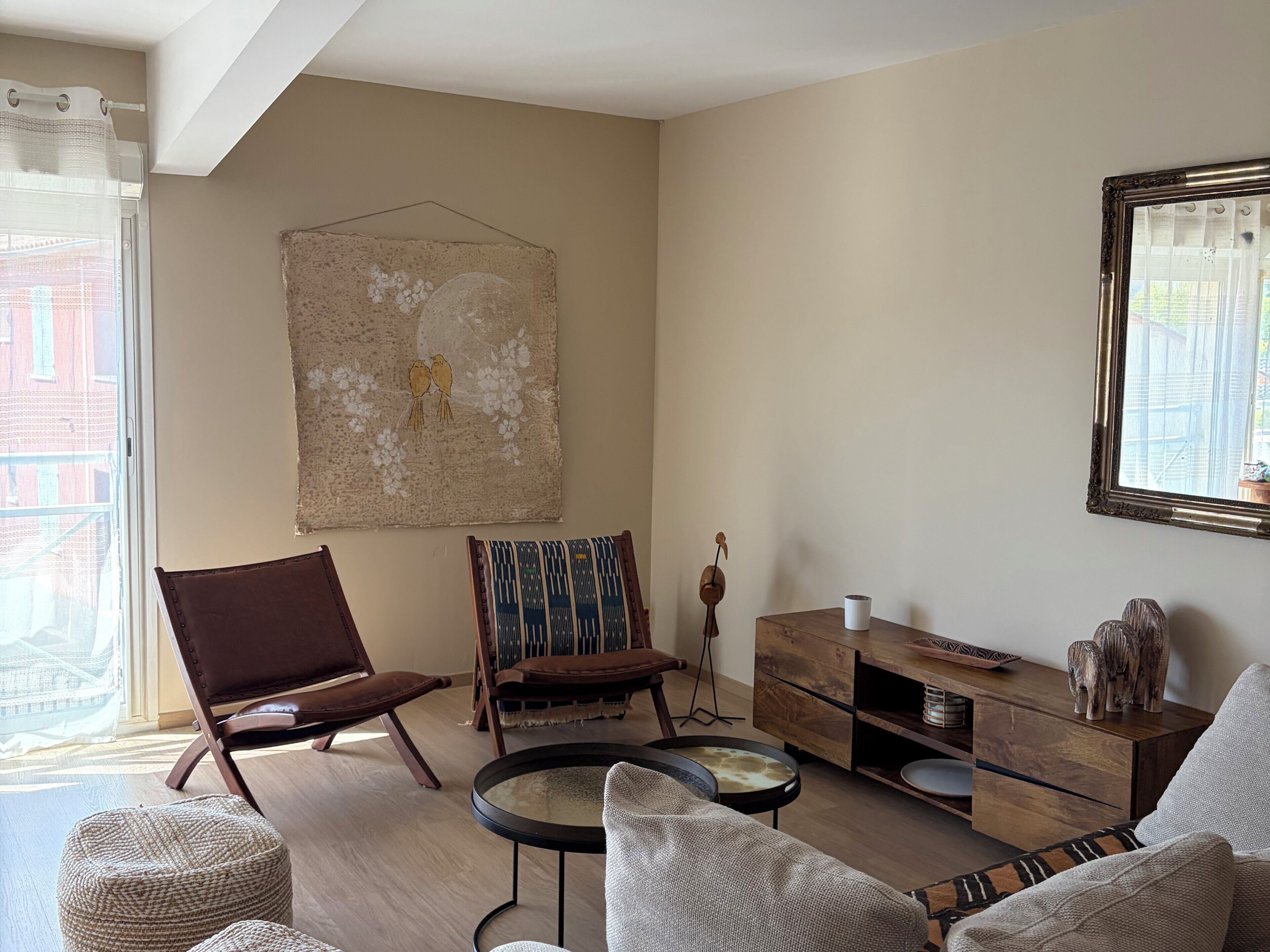 Un salon comprenant un fauteuil en cuir marron, une table basse ronde, un canapé, un meuble en bois et une œuvre d’art suspendue au mur.