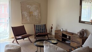 A living room with a brown leather chair, a round coffee table, a sofa, a wooden cabinet, and a hanging artwork. - Stylish Apartment - 5 Min Walk to Center (L'Isle-sur-la-Sorgue)