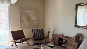 Un salon comprenant un fauteuil en cuir marron, une table basse ronde, un canapé, un meuble en bois et une œuvre d’art suspendue au mur.