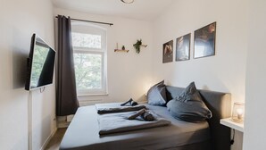 A bedroom with a bed, a TV, a window with curtains, and wall art.