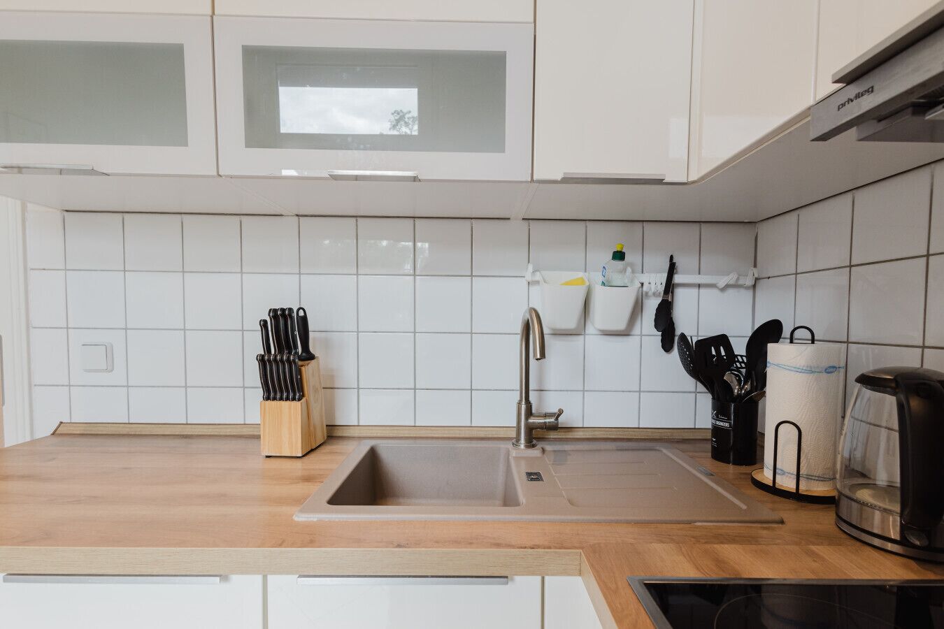 A modern kitchen with white cabinets, a stainless steel sink, and a coffee maker.