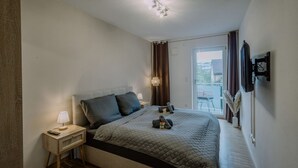 A bedroom with a bed, bedside table, lamp, and a view of the outdoors. - Passau Apartment|Singles-Couples-Groups|Central (Passau)