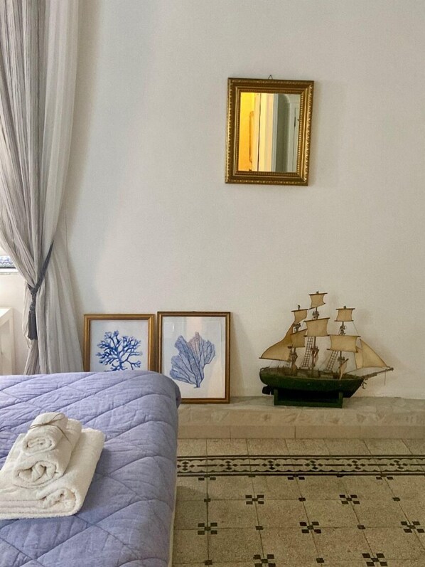 Une pièce comprenant un lit, une maquette de bateau, des œuvres d’art encadrées et un miroir au mur.