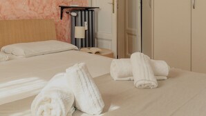A hotel room with a bed, two rolled towels, a bedside table with a lamp, and a radiator. - JOIVY Bright flat near the city centre  (Milan)