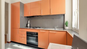 A modern kitchen with orange cabinets, a stainless steel range hood, a built-in oven, and a sink. - JOIVY Bright flat near the city centre  (Milan)