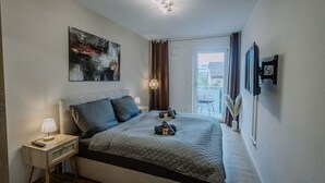 Une chambre à coucher moderne avec un grand lit, une table de chevet, un tableau et une vue sur l’extérieur.