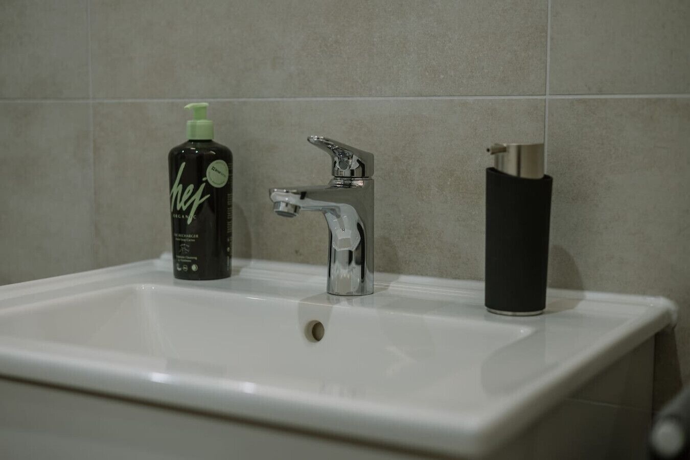 A bathroom sink with a chrome faucet and a bottle of organic hand soap.