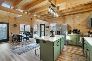 A wooden cabin interior with a dining area, kitchen, and large windows.