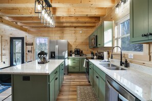 A modern kitchen with wooden beams, green cabinets, a large island, and a view of the outdoors.