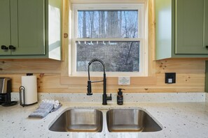 A kitchen with two stainless steel sinks, a window with a view of trees, and wooden cabinets.