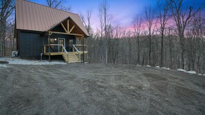A rustic cabin with a metal roof and wooden deck, surrounded by a forested area. - Timberline Retreat | Hocking Hills, Hot Tub (Creola)